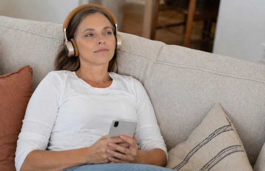 Femeie relaxându‑se pe canapea cu căști, în timpul unei ședințe personalizate de bătăi binaurale
